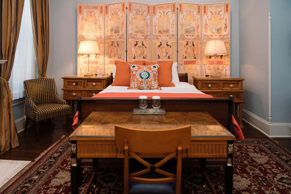 Straight-on view of a bedroom suite featuring a wooden desk in the foreground, a sleigh bed with orange accents, and a large decorative screen behind the headboard.