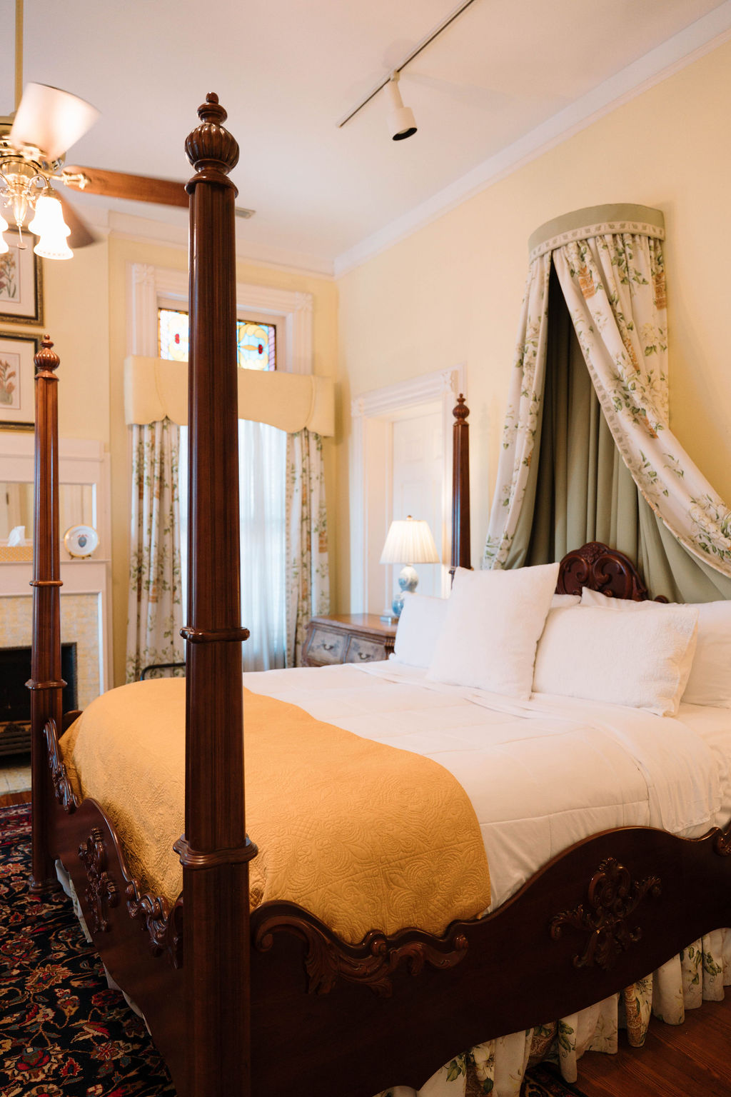 Elegant bedroom suite featuring a dark wood four-poster bed with a floral crown canopy, a gold throw blanket, and tall windows.