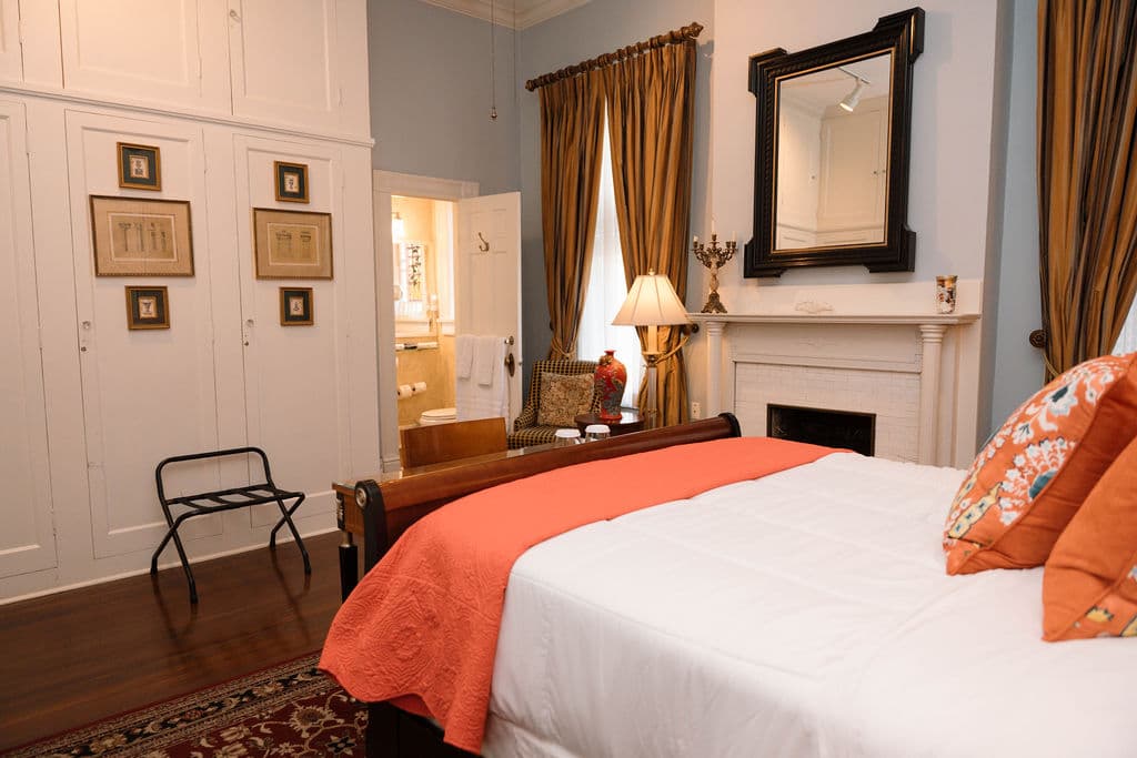Bedroom suite featuring a bed with orange accents, a white fireplace, a wall of built-in closets, and an open doorway to the bathroom.