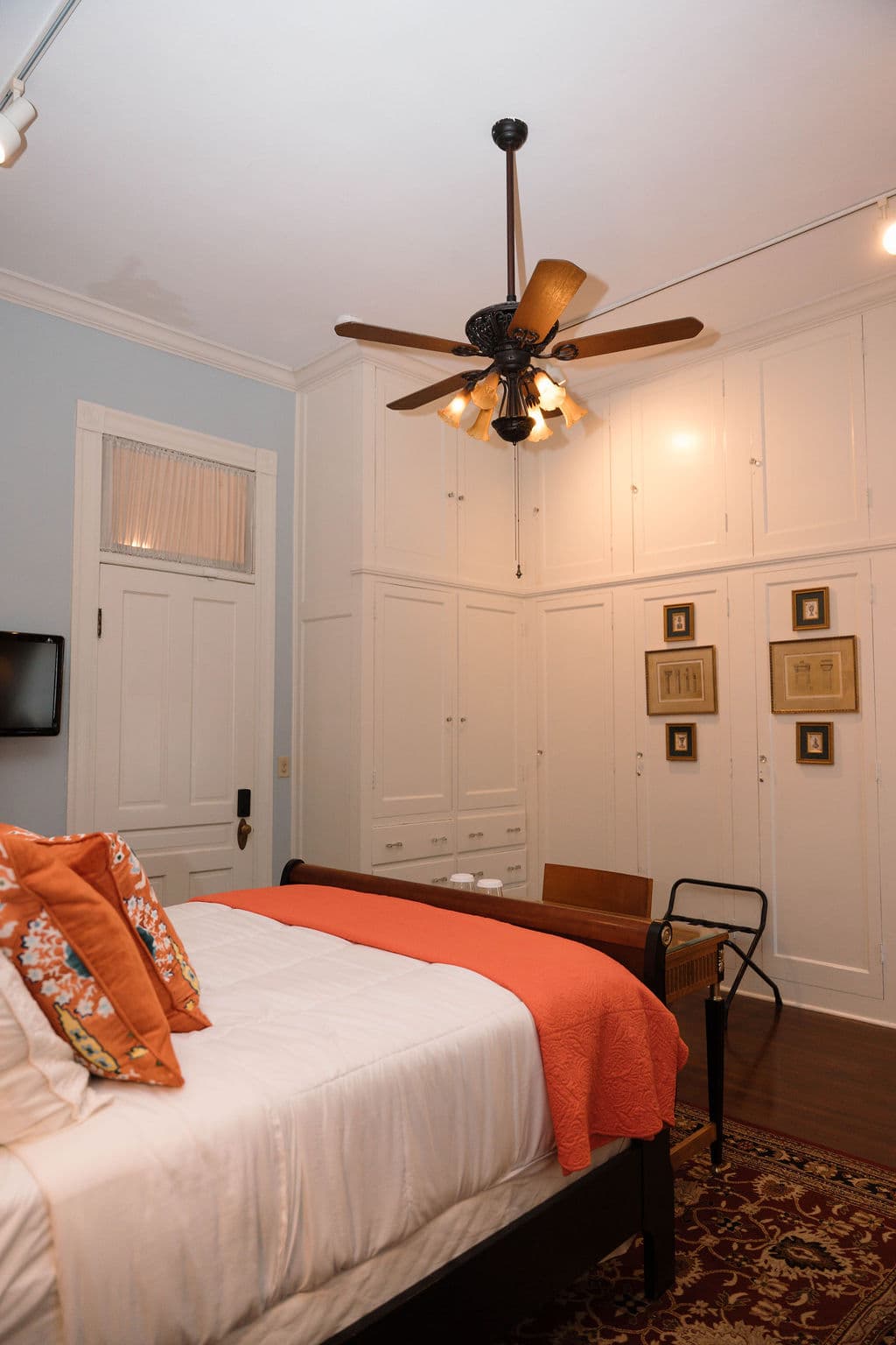 Bedroom suite featuring a sleigh bed with orange pillows and throw, a ceiling fan, and a wall of white floor-to-ceiling built-in closets.