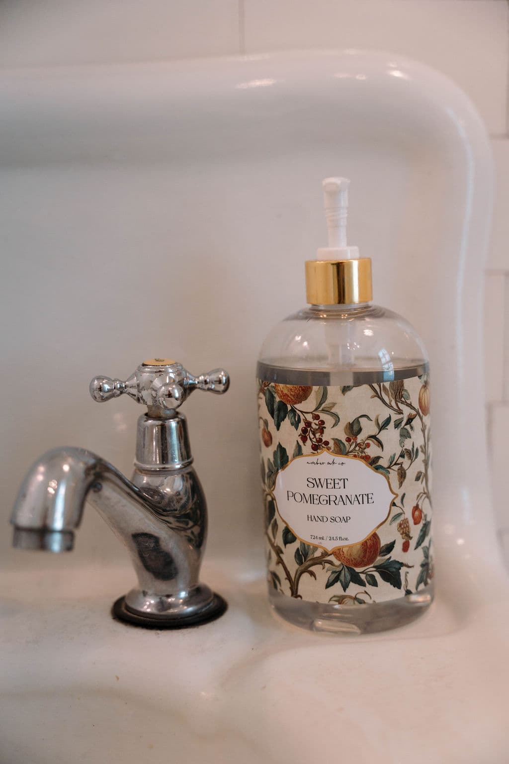 Close-up of a vintage chrome faucet and a decorative bottle of Sweet Orange hand soap resting on a white porcelain sink.
