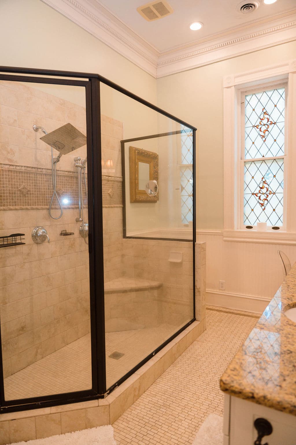 Modern bathroom suite featuring a spacious glass-enclosed walk-in shower with a built-in bench, granite vanity, and a decorative diamond-patterned window.