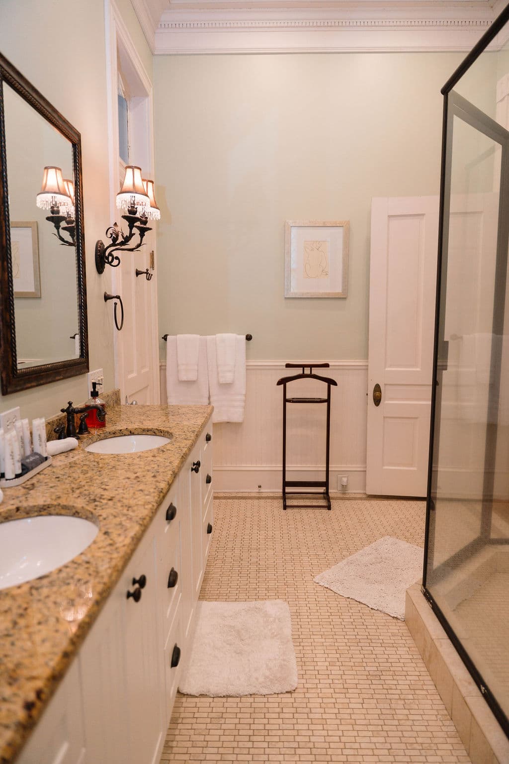Spacious bathroom suite featuring a long granite double vanity, a glass-enclosed shower, mosaic tile flooring, and a freestanding towel valet.