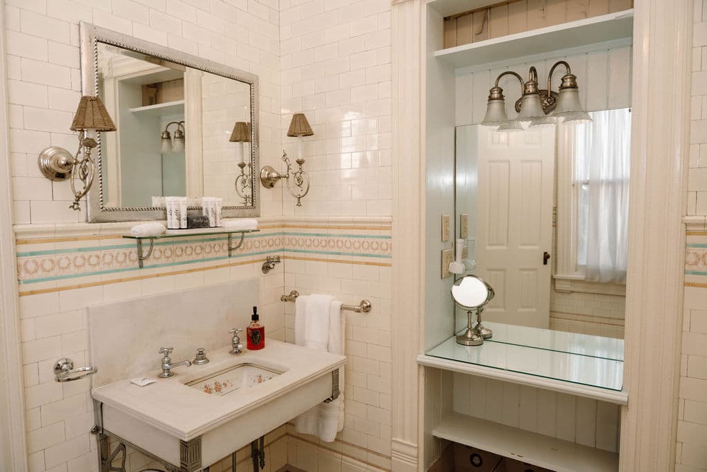 Classic bathroom interior with a console sink, silver vanity mirror, and built-in mirrored alcove.