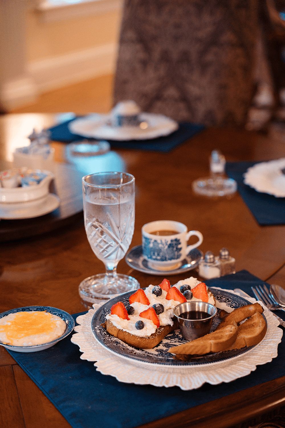 A beautifully arranged breakfast plate with French toast topped with strawberries and blueberries, served alongside a glass of water and coffee.