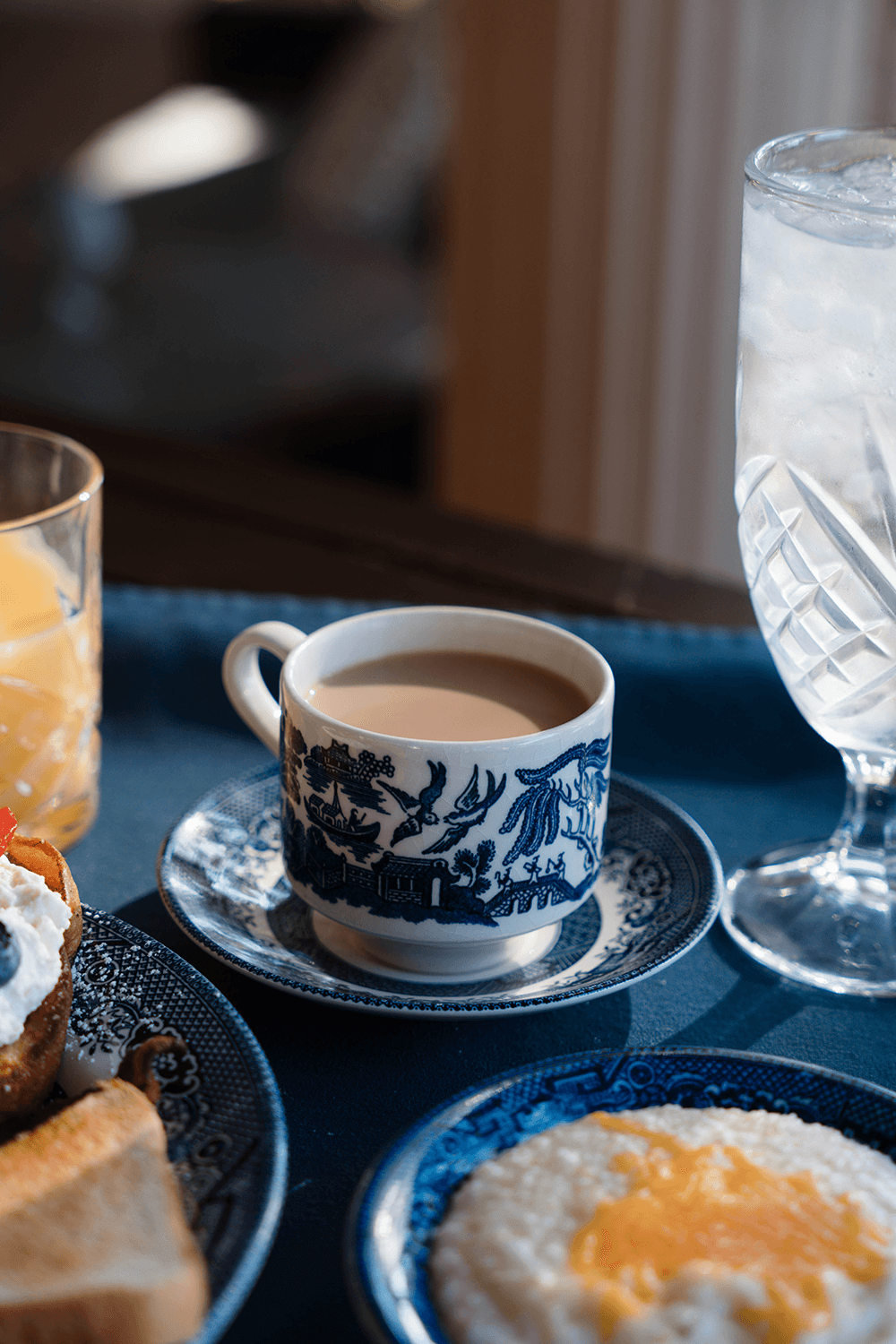 A beautifully arranged breakfast tray with a cup of coffee, a glass of iced water, orange juice, toast, and a bowl of creamy grits topped with an egg yolk.