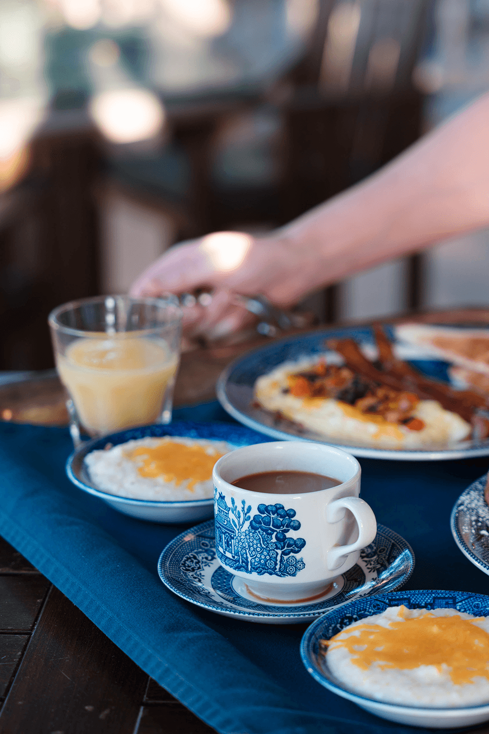 A breakfast spread featuring coffee, orange juice, omelette, bacon, and grits on decorative plates.
