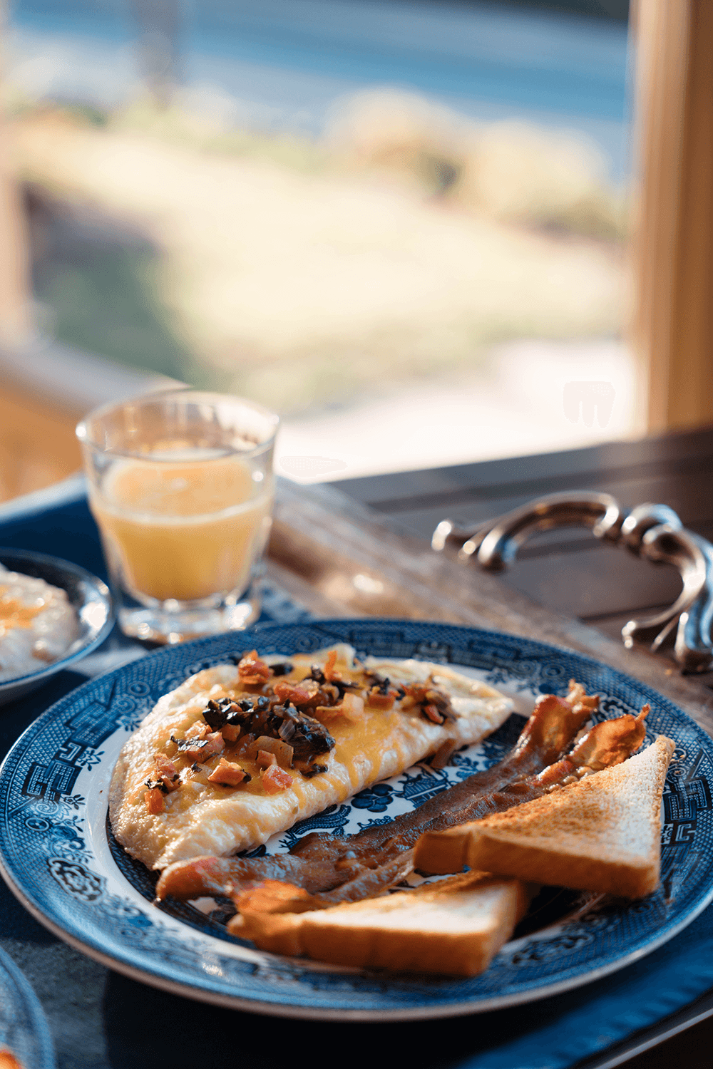 A plate of omelette topped with vegetables, bacon, and toast, accompanied by a glass of orange juice.