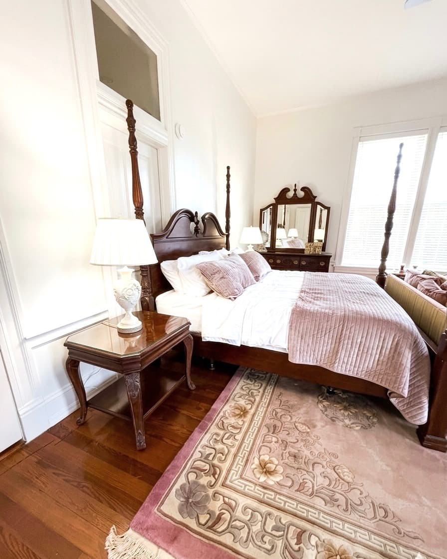A cozy bedroom featuring a wooden four-poster bed, elegant lamps, and a vintage area rug.